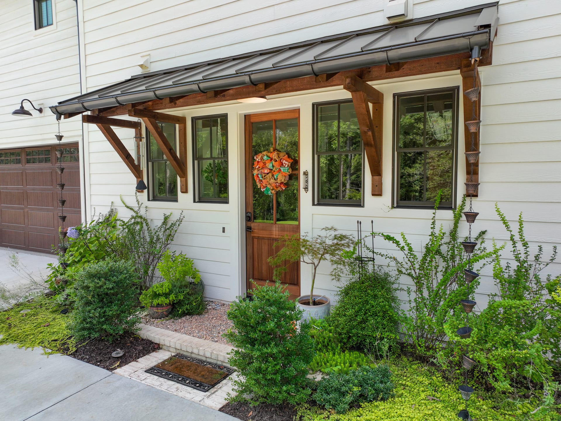 Side entry with metal awning and garden plantings — a quiet arrival.