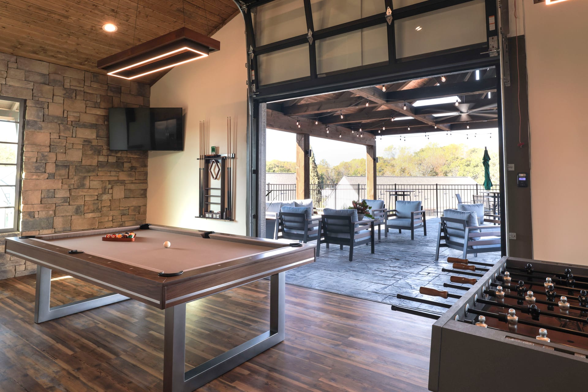Stone accent wall frames the game room — pool table, foosball, and cabana views.