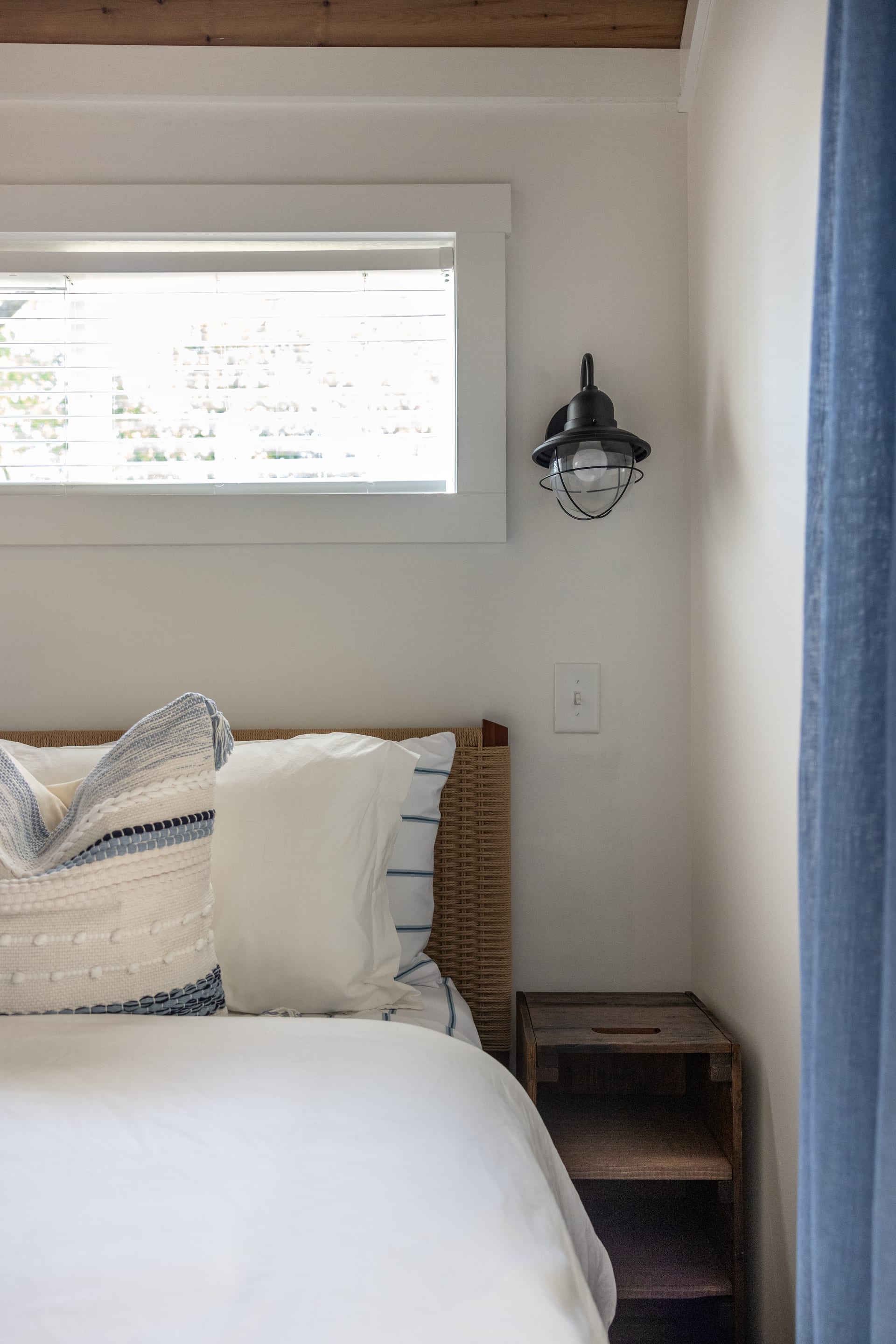 Nautical cage sconce and woven headboard whisper coastal comfort.