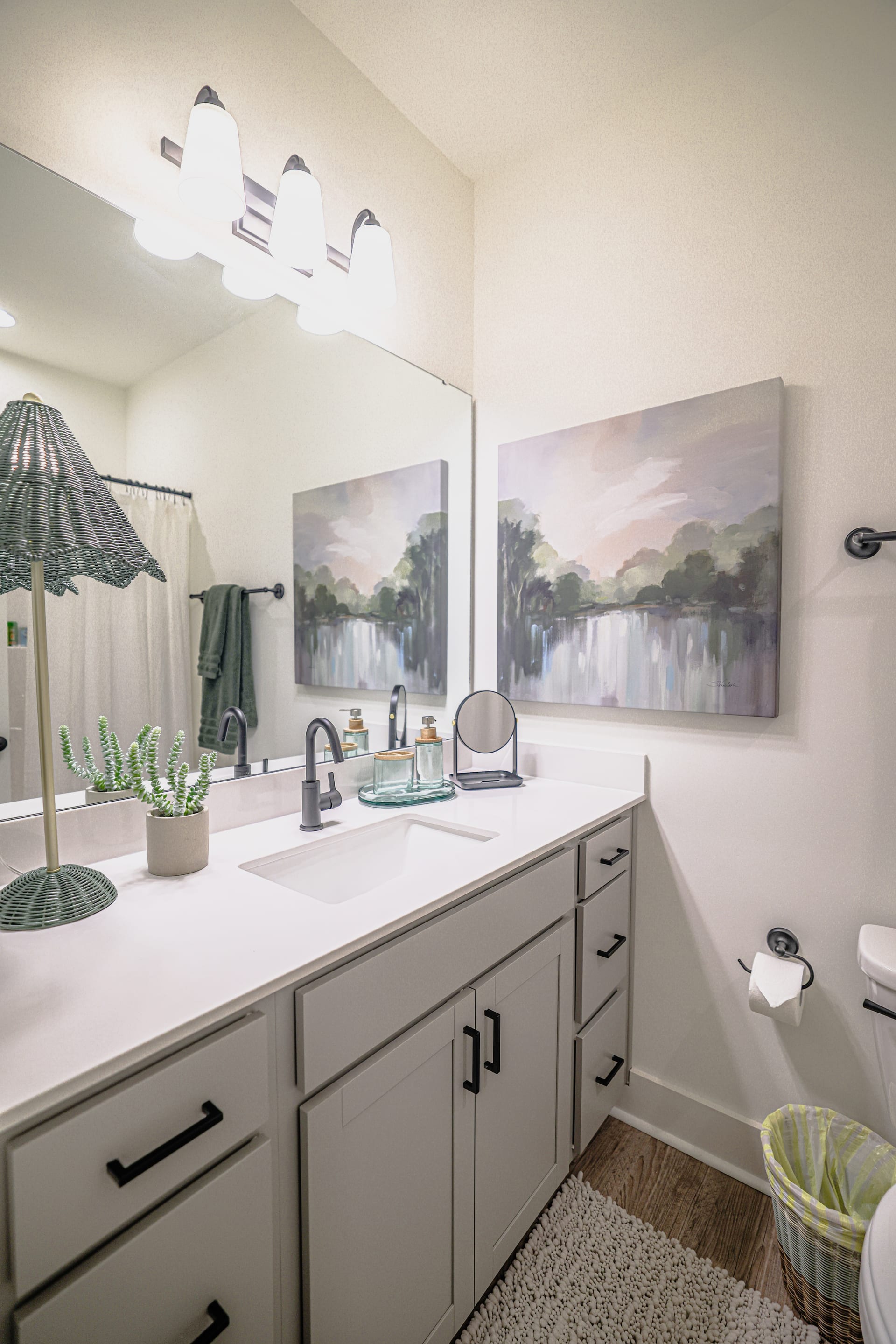Grey vanity and a green lamp beside a lake canvas set a tranquil tone.