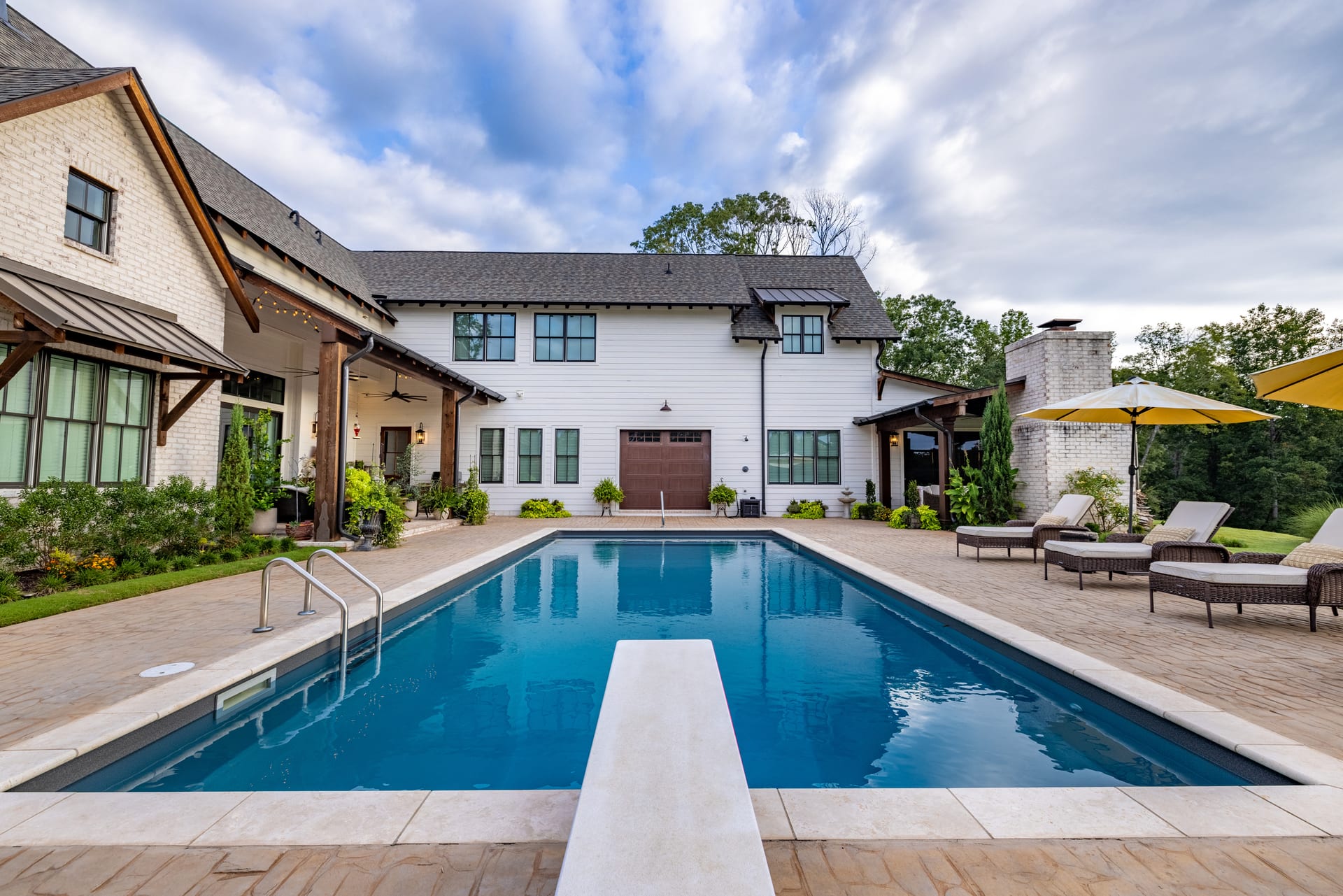 Diving board and paver deck stretch beneath the farmhouse rear facade.